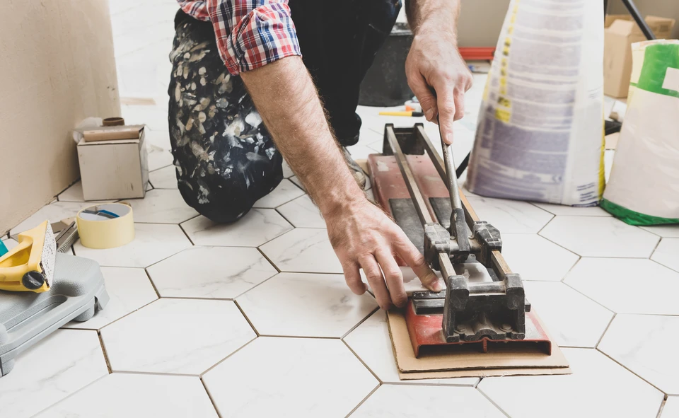 Ouvrier en combinaison bleue et casque jaune utilisant une scie circulaire électrique pour découper du carrelage dans un chantier de rénovation intérieure